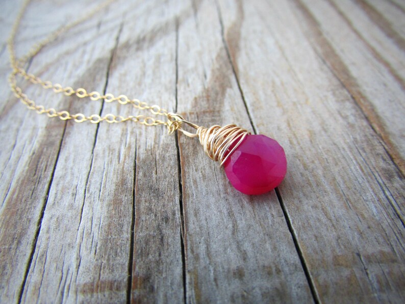 May include: A gold chain necklace with a pink gemstone pendant wrapped in gold wire.