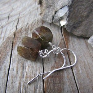 May include: A pair of silver earrings with green gemstone cube dangles. The earrings have a simple, minimalist design.