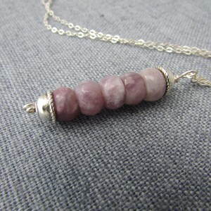 May include: A silver chain necklace with a pendant made of five round, light pink and white stones. The stones are set in silver.
