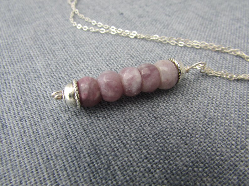 May include: A silver chain necklace with a pendant made of five round, light pink and white stones. The stones are set in silver.