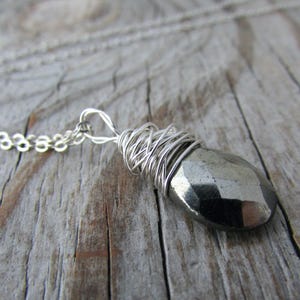 Può includere: Una collana a catena d'argento con un ciondolo in pirite avvolto in filo d'argento. Il ciondolo è una pietra sfaccettata di colore grigio scuro.