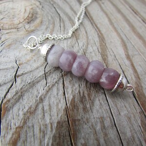 May include: A silver chain necklace with a pendant made of five round, light purple gemstone beads. The beads are graduated in size, with the largest bead at the bottom.