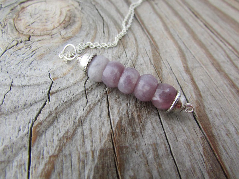 May include: A silver chain necklace with a pendant made of five round, light purple gemstone beads. The beads are graduated in size, with the largest bead at the bottom.