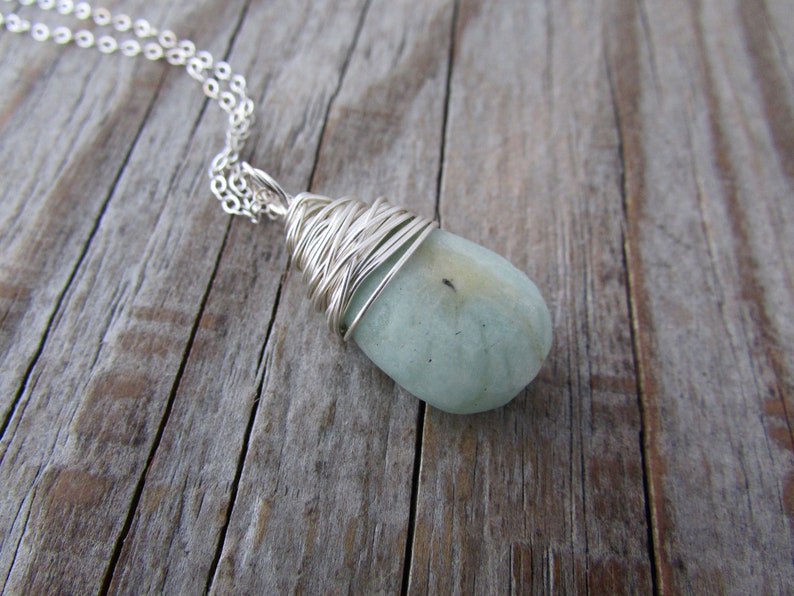 Pu&ograve; includere: Una collana con catena d'argento con un ciondolo di pietra preziosa blu chiaro avvolto in filo d'argento.