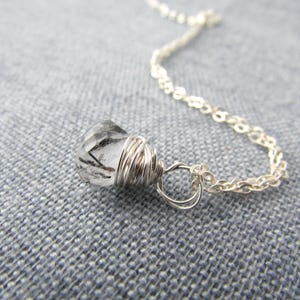 May include: A silver chain necklace with a clear quartz crystal pendant wrapped in silver wire.