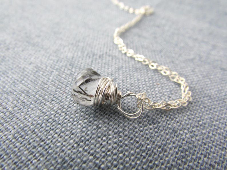 May include: A silver chain necklace with a clear quartz crystal pendant wrapped in silver wire.