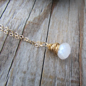 May include: A gold chain necklace with a white gemstone pendant wrapped in gold wire.