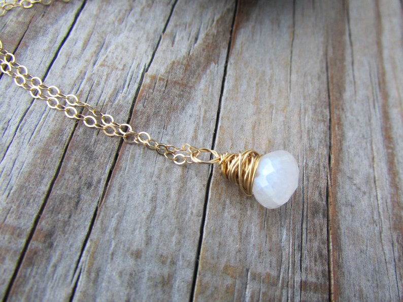 May include: A gold chain necklace with a white gemstone pendant wrapped in gold wire.