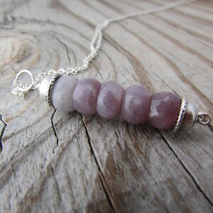 May include: A silver chain necklace with a pendant made of six round, light purple beads. The beads are separated by silver spacers.