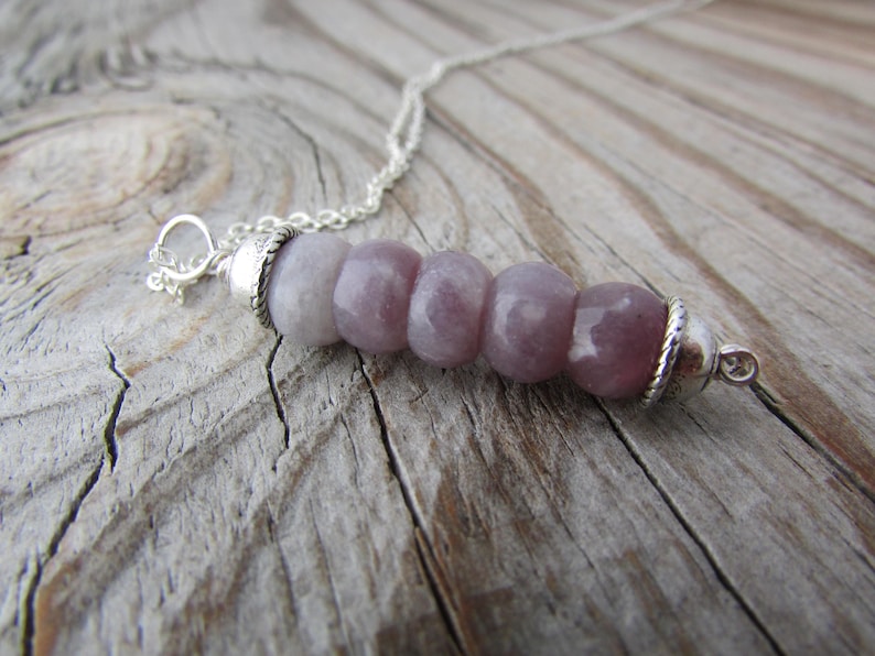 May include: A silver chain necklace with a pendant made of six round, light purple beads. The beads are separated by silver spacers.