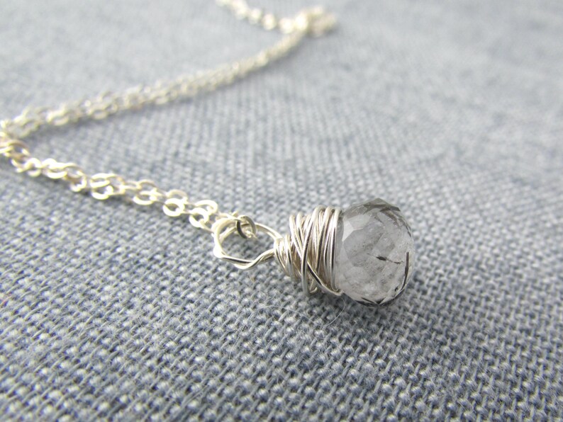 May include: A silver chain necklace with a clear quartz crystal wrapped in silver wire.