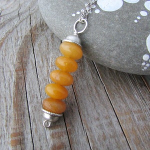May include: A silver chain necklace with a pendant made of five stacked, smooth, yellow-orange stones. The pendant is attached to the chain with a silver clasp.