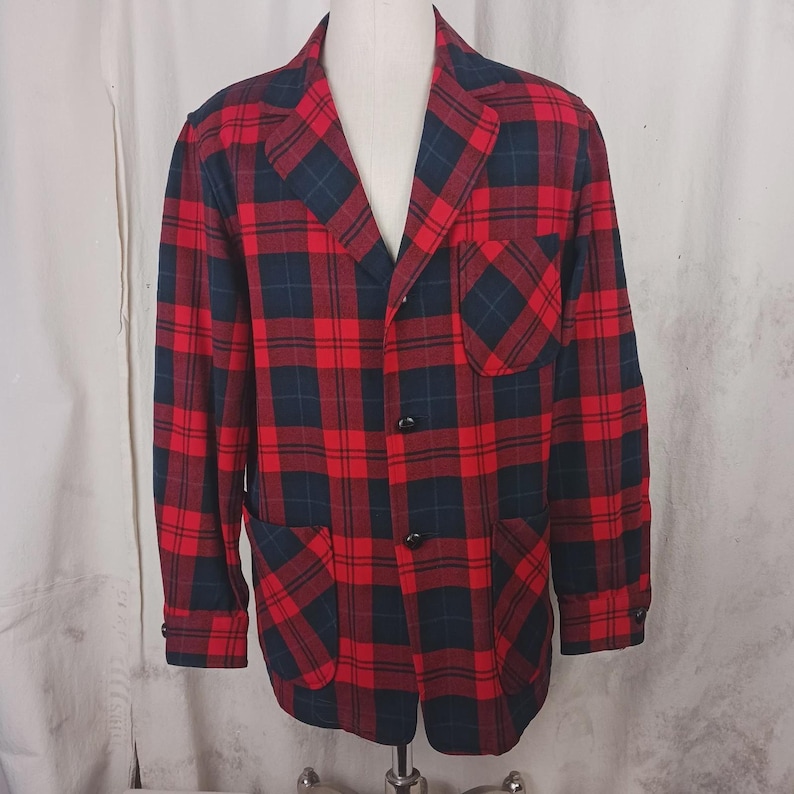 May include: A red and navy plaid blazer with two front pockets and three black buttons. The blazer is displayed on a mannequin. The plaid pattern is a classic design.