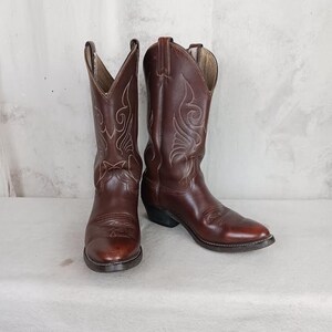 May include: A pair of brown leather cowboy boots with intricate stitching designs. The boots have a pointed toe and a slight heel.