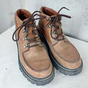 May include: A pair of brown leather ankle boots with laces and metal eyelets. The boots have a rugged, outdoor look.
