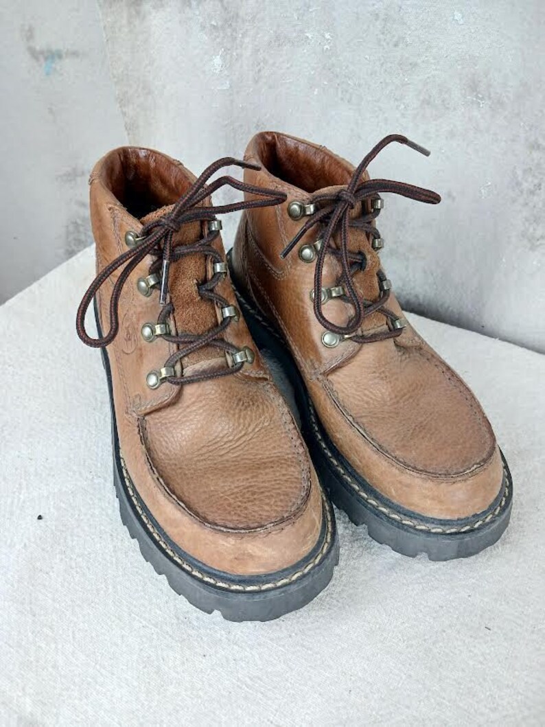 May include: A pair of brown leather ankle boots with laces and metal eyelets. The boots have a rugged, outdoor look.