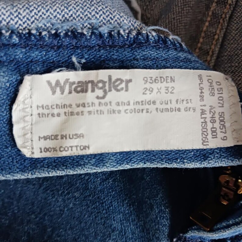 May include: A white Wrangler jeans care label with the text "Wrangler 936DEN 29 x 32", "Machine wash hot and inside out first three times with like colors, tumble dry", "MADE IN USA", "100% COTTON".