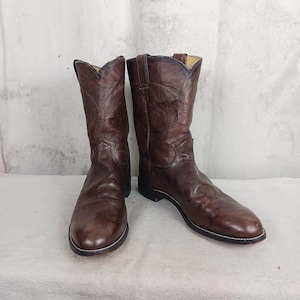May include: A pair of brown leather cowboy boots with a pointed toe and a slight heel. The boots are made of a textured leather and have a classic cowboy boot design.