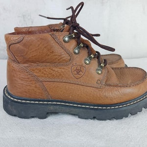 May include: Brown leather hiking boots with a lace-up closure and a brand logo on the side. The boots have a rugged outsole and a comfortable fit.