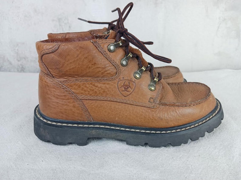 May include: Brown leather hiking boots with a lace-up closure and a brand logo on the side. The boots have a rugged outsole and a comfortable fit.