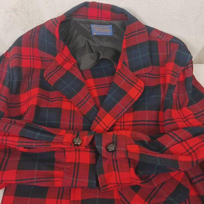 May include: A red and black plaid blazer with a classic design. The jacket features a notched collar, two buttons on the front, and buttons on the sleeves. The interior lining is black.