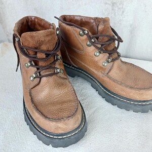 May include: A pair of brown leather ankle boots with laces and metal eyelets. The boots have a thick rubber sole.