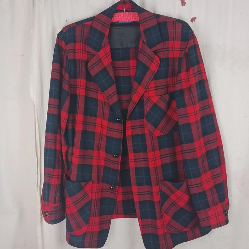 May include: A red and navy plaid blazer with two front pockets and three buttons. The blazer has a classic design and is made of a woven fabric. The jacket is hanging on a hanger.