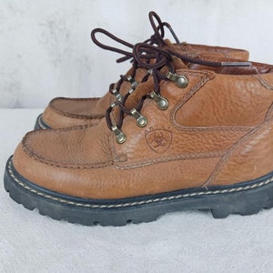 May include: Brown leather hiking boots with a lace-up closure and a logo on the side. The boots have a rugged outsole.