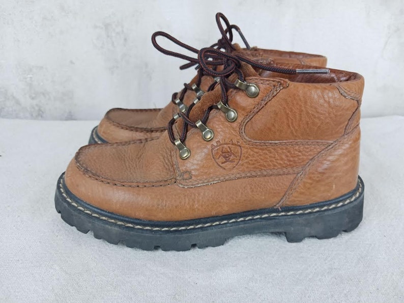 May include: Brown leather hiking boots with a lace-up closure and a logo on the side. The boots have a rugged outsole.
