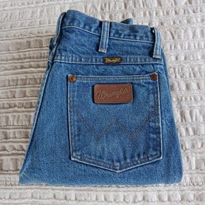 May include: A pair of blue denim jeans with a brown leather patch that says "Wrangler" on the back pocket.