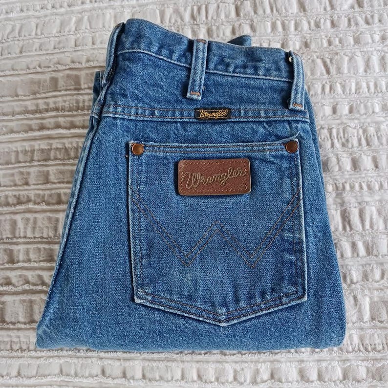 May include: A pair of blue denim jeans with a brown leather patch that says "Wrangler" on the back pocket.