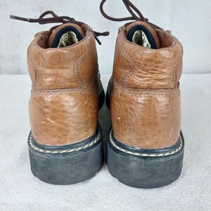 May include: A pair of brown leather ankle boots with black laces and a black rubber sole. The boots have a stitched seam around the top of the sole.
