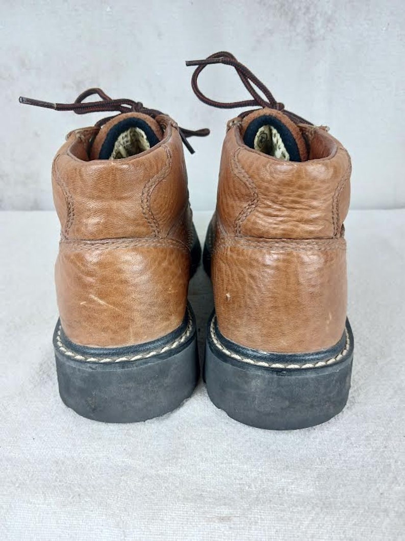 May include: A pair of brown leather ankle boots with black laces and a black rubber sole. The boots have a stitched seam around the top of the sole.