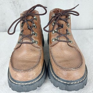 May include: A pair of brown leather ankle boots with laces and metal eyelets. The boots have a thick black rubber sole with a stitched edge.