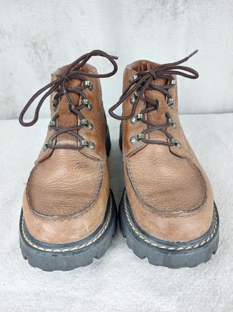 May include: A pair of brown leather ankle boots with laces and metal eyelets. The boots have a thick black rubber sole with a stitched edge.