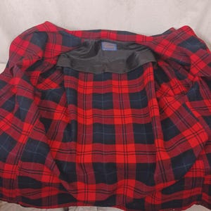 May include: Open view of a red and black plaid jacket. The interior lining features a bold red and black plaid pattern. The jacket's collar is black, and a small label is visible at the top.