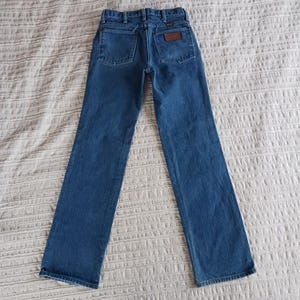 May include: A pair of blue denim jeans with a brown leather patch on the back pocket that says "Wrangler".