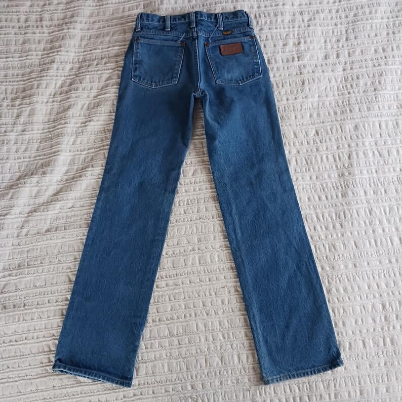 May include: A pair of blue denim jeans with a brown leather patch on the back pocket that says "Wrangler".