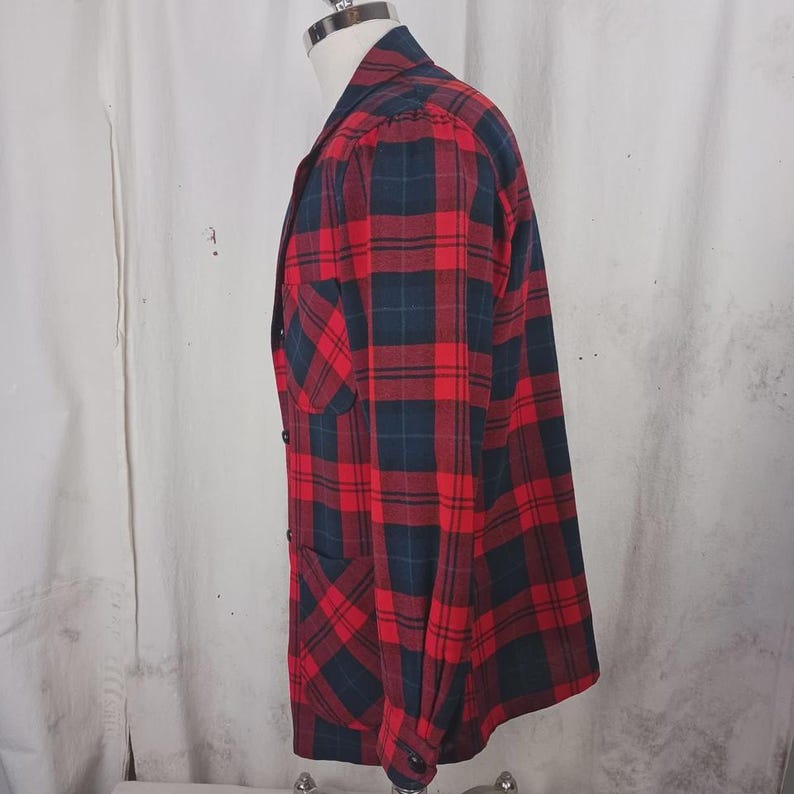 May include: Red and navy blue plaid flannel shirt with a button-down front, a chest pocket, and long sleeves. The shirt is displayed on a mannequin. The fabric has a classic lumberjack style pattern.