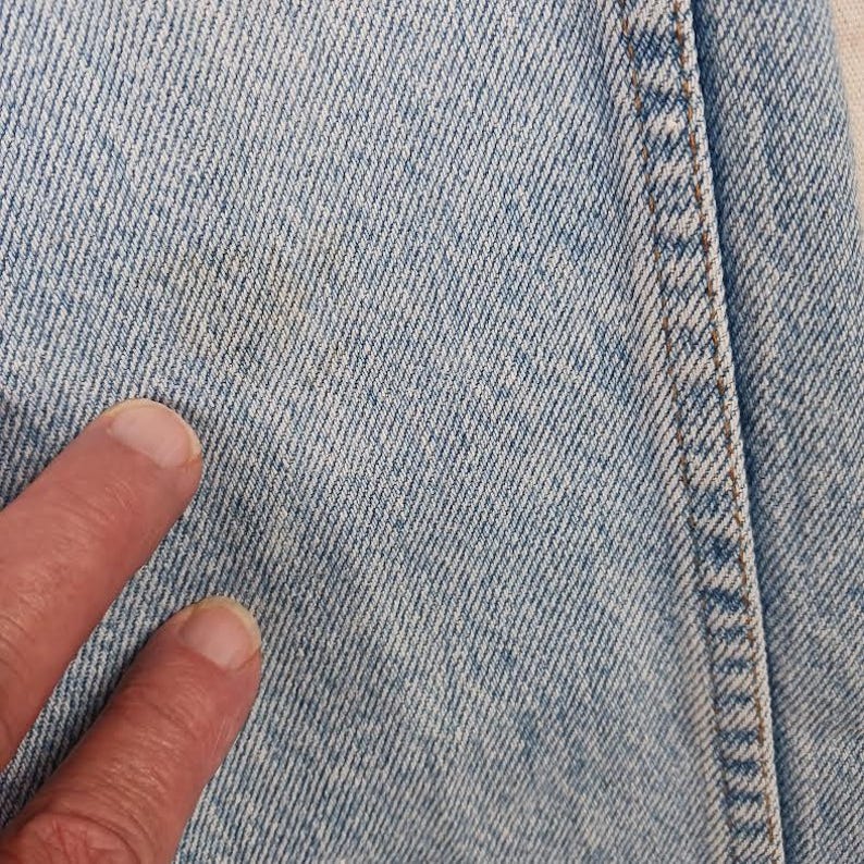 Puede incluir: Primer plano de tejido vaquero azul claro con una sola costura que recorre verticalmente el lado derecho de la imagen.