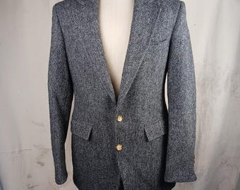 May include: A gray tweed blazer with a two-button closure and two front pockets. The blazer has a notched lapel and gold-colored buttons. The jacket is displayed on a mannequin.
