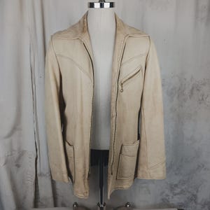 May include: Cream-colored leather jacket with a zip-up front, two front pockets, and a small zippered chest pocket. The jacket has a classic collar and decorative stitching details. The jacket is displayed on a mannequin.