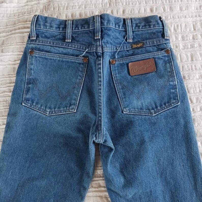 May include: A pair of blue denim jeans with a brown leather patch that says "Wrangler" on the back pocket.