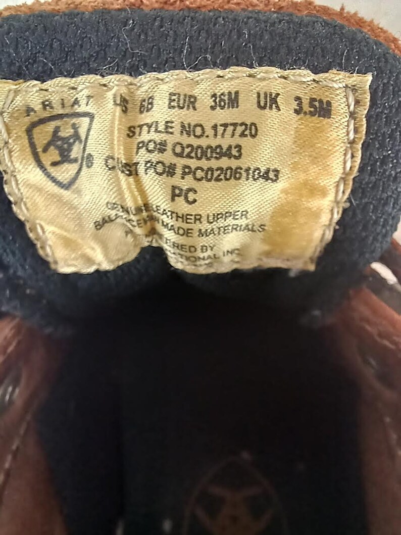 May include: Brown leather Ariat boot with a size tag that reads "68 EUR 36M UK 3.5M", "STYLE NO. 17720", "PO# Q200943", "CUST PO# PC02061043", "PC", "GENUINE LEATHER UPPER", "BALANCES MADE MATERIALS", "ERED BY", "TIONAL INC".