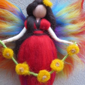 Könnte beinhalten: Eine Filz-Feenpuppe mit Regenbogenflügeln, einem roten Kleid und einer Blumenkrone. Die Fee hält eine Schnur mit gelben Filzblumen.