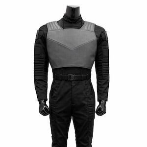 May include: A black tactical jumpsuit with a grey chest plate and a black belt. The outfit includes black combat boots. The mannequin is on a white background. The jumpsuit has ribbed detailing on the arms and legs.