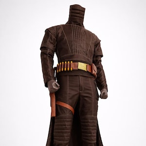 Puede incluir: Un disfraz marr&oacute;n con una chaqueta de cuello alto, pantalones y botas. La chaqueta tiene costuras verticales y los pantalones tienen secciones de rodilla acolchadas. Un cintur&oacute;n marr&oacute;n con detalles dorados y una funda completan el atuendo.