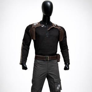 May include: Black costume displayed on a mannequin. The outfit includes a long-sleeved black shirt, gray pants with cargo pockets, and a brown leather harness with pouches. A brown belt and black boots complete the ensemble.
