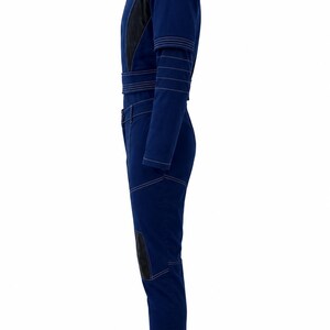 May include: A dark blue jumpsuit with black accents and white stitching. The jumpsuit features a high collar, long sleeves, and a belt at the waist. Black patches are on the knees. The overall design is sleek and modern.