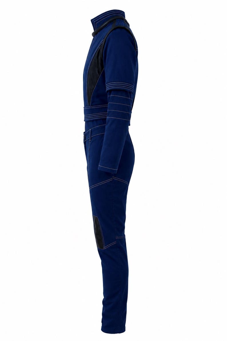 May include: A dark blue jumpsuit with black accents and white stitching. The jumpsuit features a high collar, long sleeves, and a belt at the waist. Black patches are on the knees. The overall design is sleek and modern.